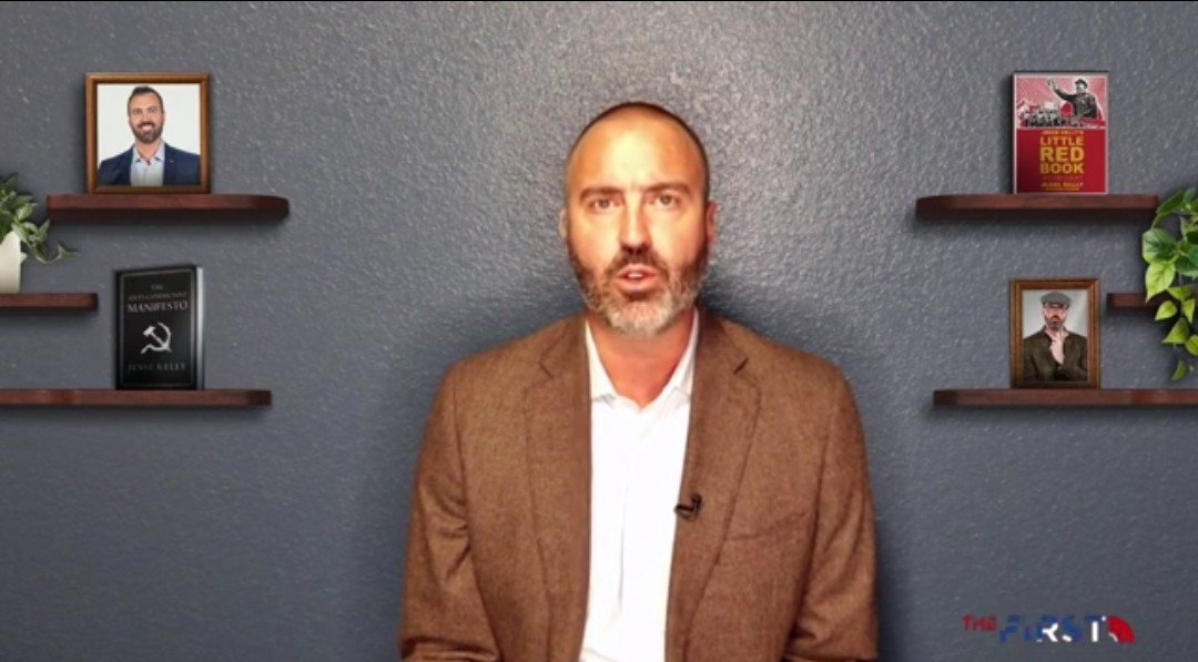 Man in a brown blazer speaking against a blue wall, with books and framed photos on shelves behind him, conveying a professional and engaging atmosphere.