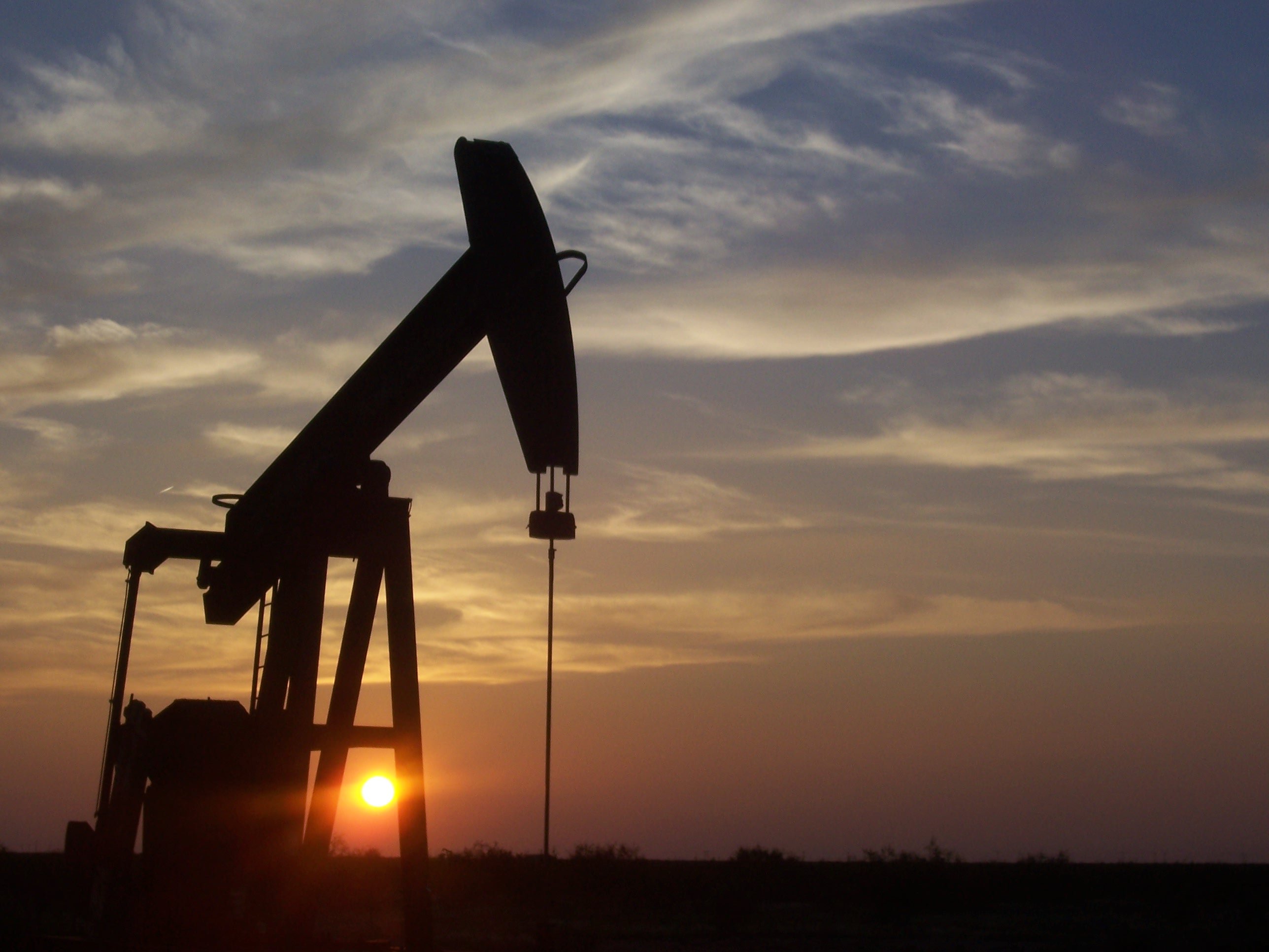 Silhouette of an oil pump jack against a colorful sunset sky, highlighting the energy industry and its environmental impact.