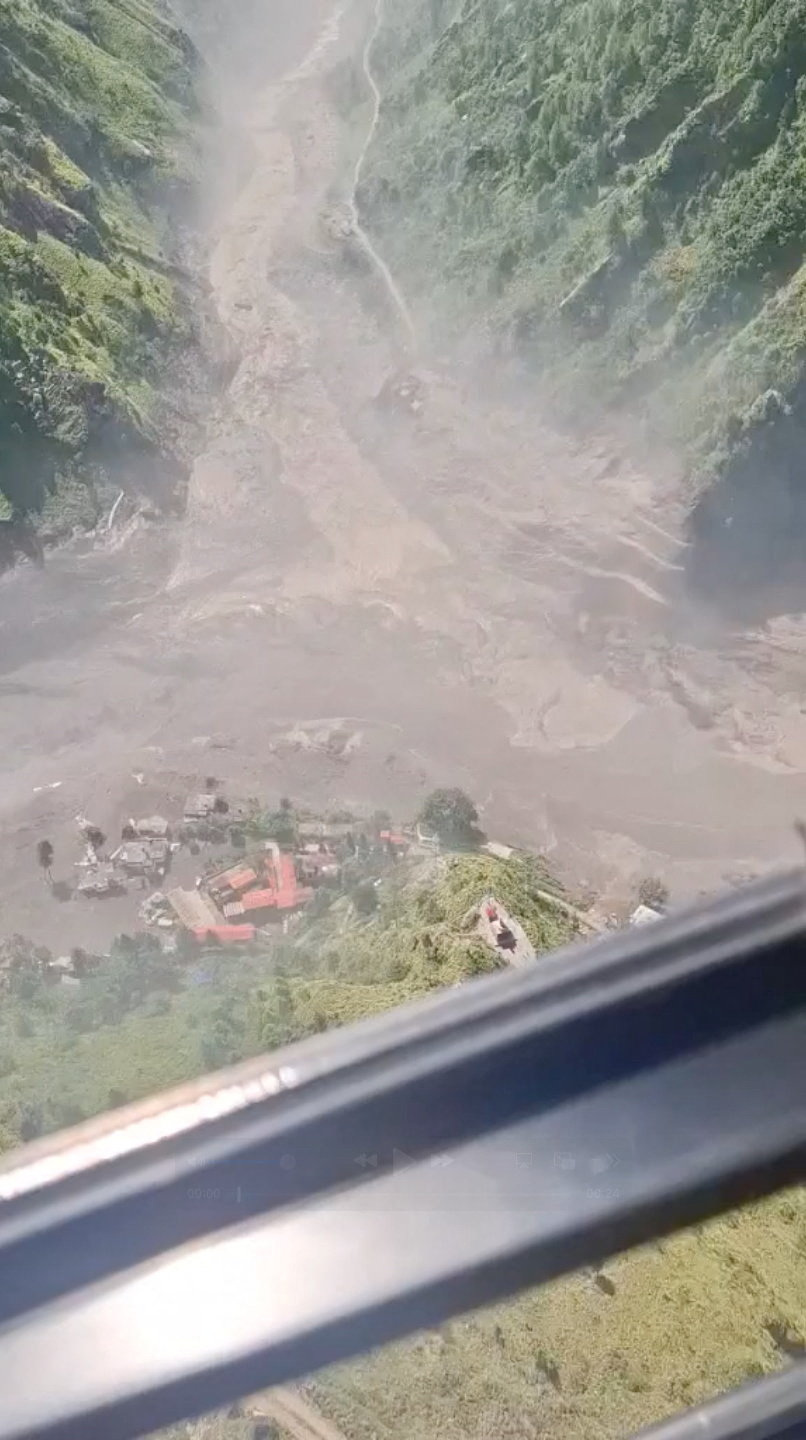 Aerial view of a mudslide engulfing a small village settlement in a mountain valley in Rasuwa, Nepal, seen through a helicopter window.