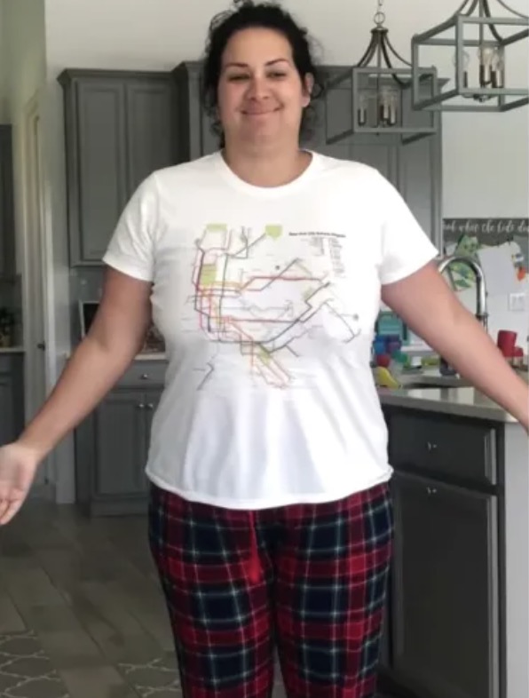 Smiling woman in a white graphic t-shirt and red plaid pants standing in a gray kitchen.