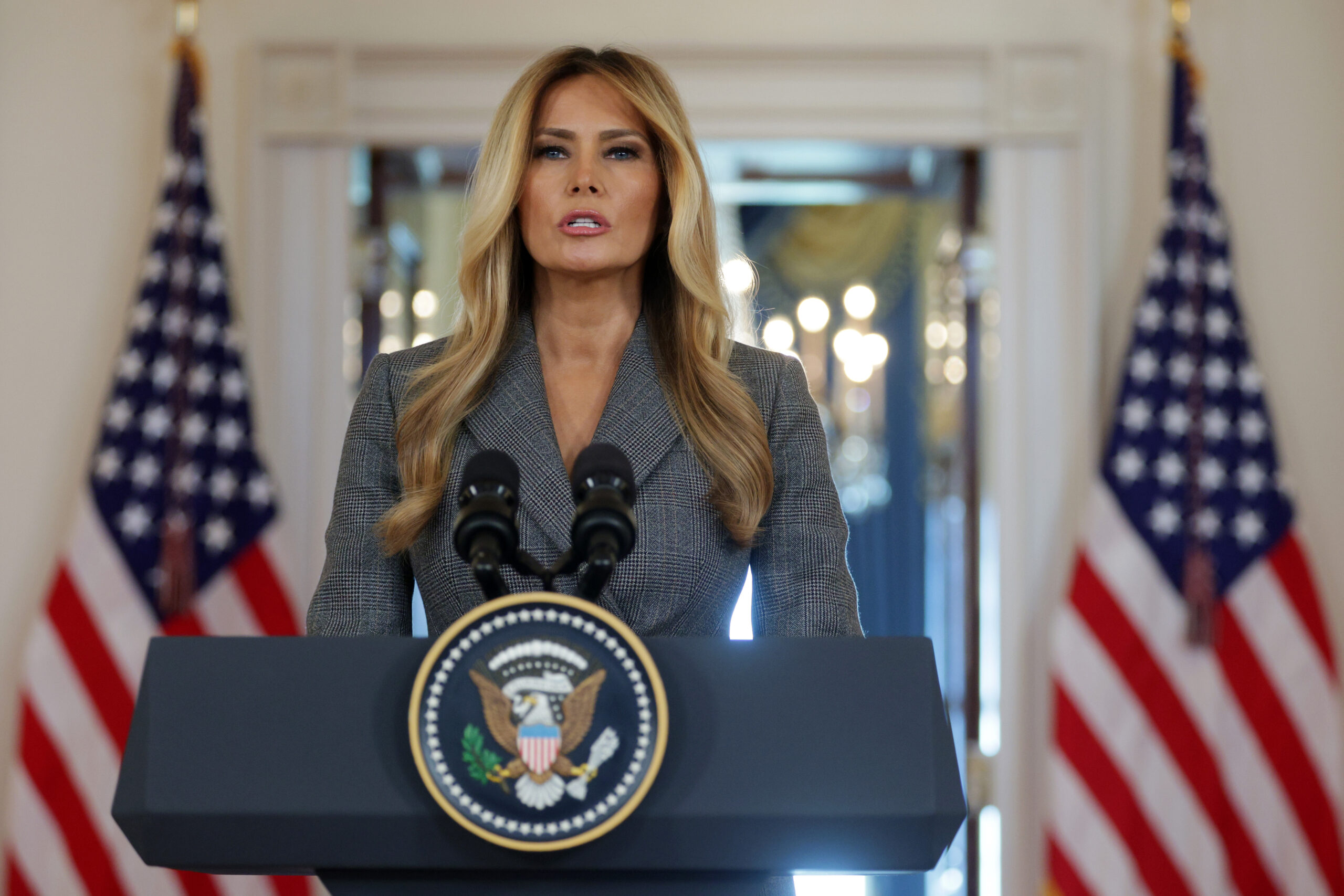 Melania Trump speaking at a podium in the Grand Foyer of the White House