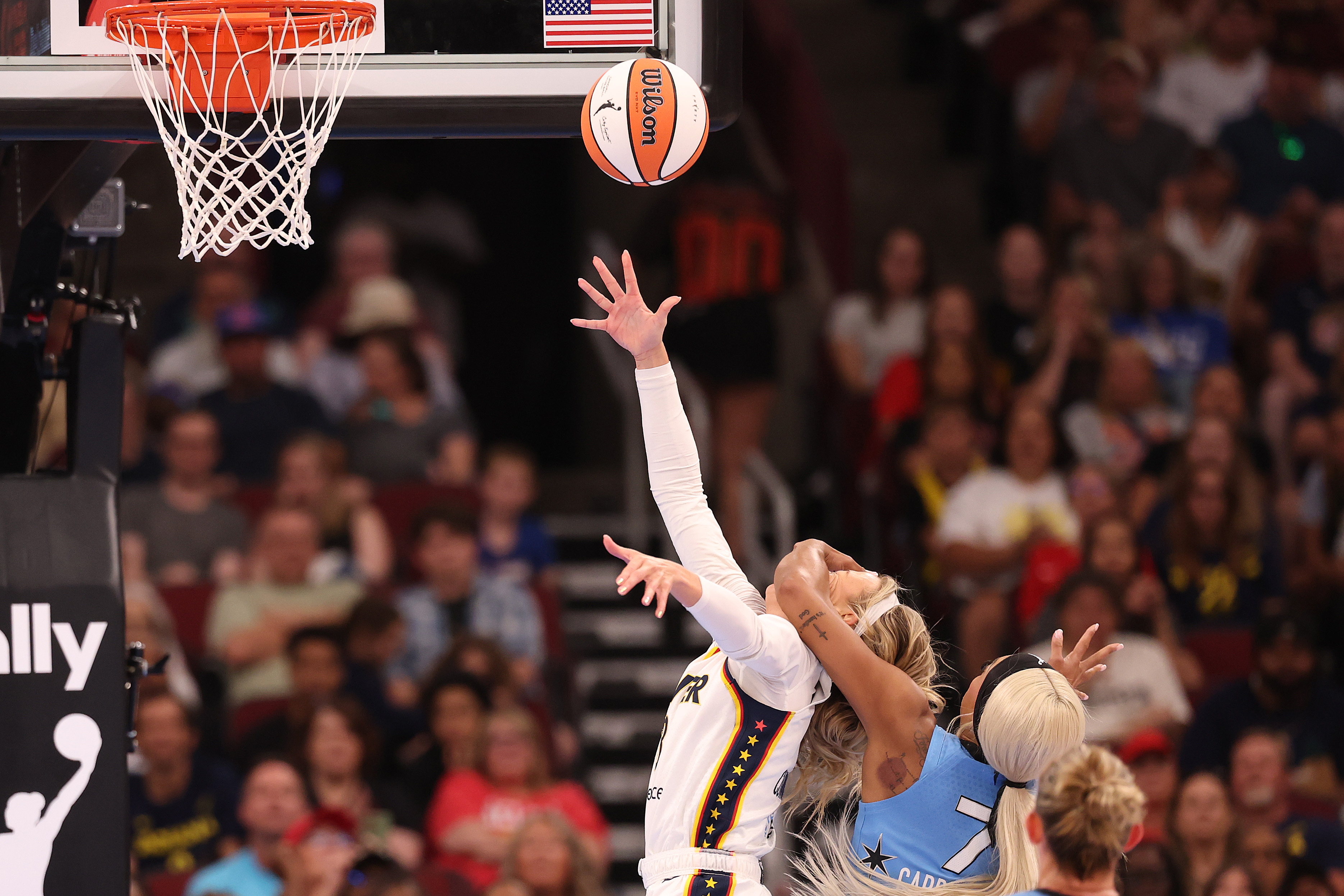 Indiana Fever player Sophie Cunningham reaches for a layup while being fouled by a Chicago Sky defender near the basket.