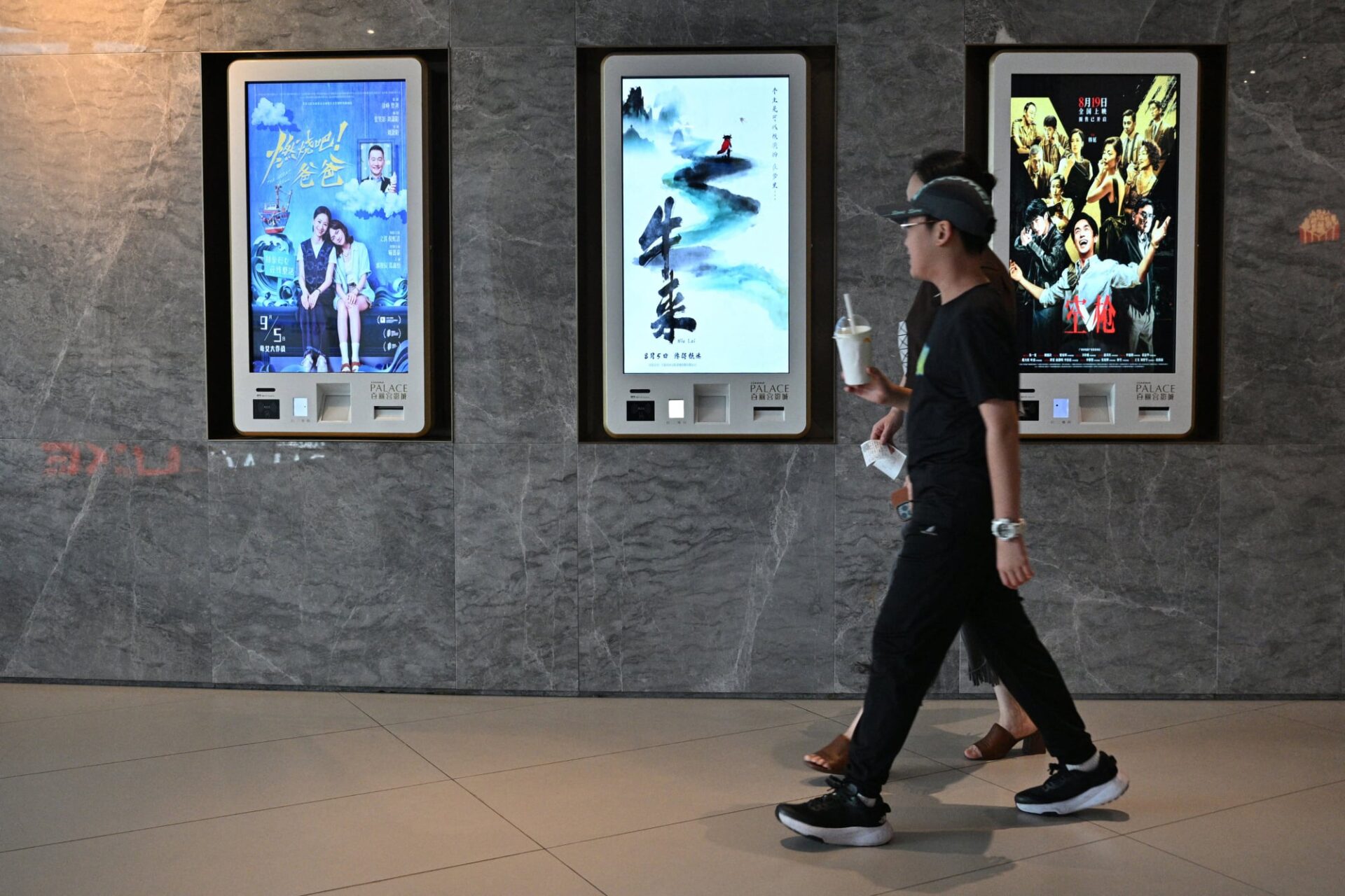 People walk past ticket machines advertising films including "Niu Lai" (C), which translates to "Here Comes the Cow", at a cinema in Shanghai on August 21, 2026.