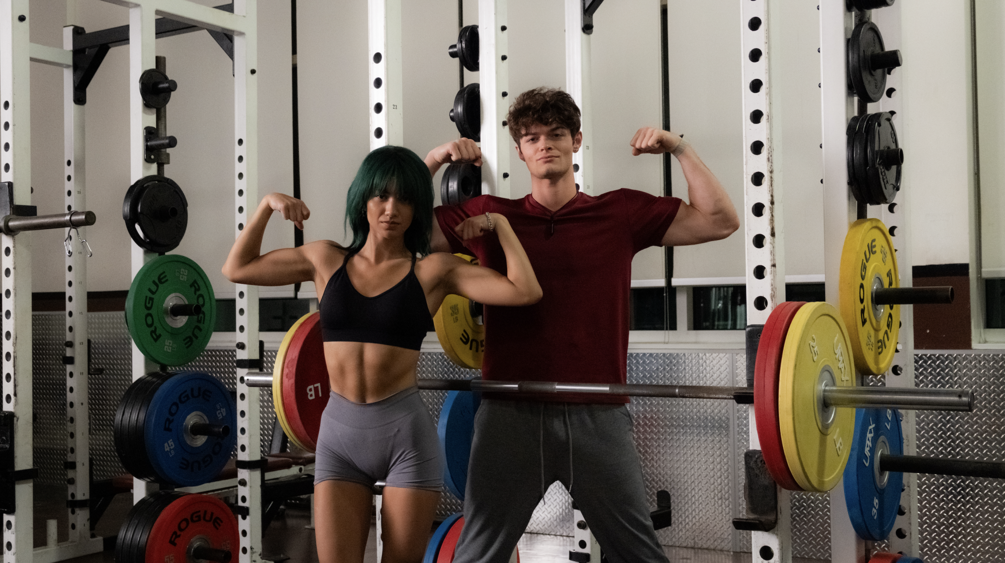 A young woman with green hair works out and flexes her muscles alongside young man