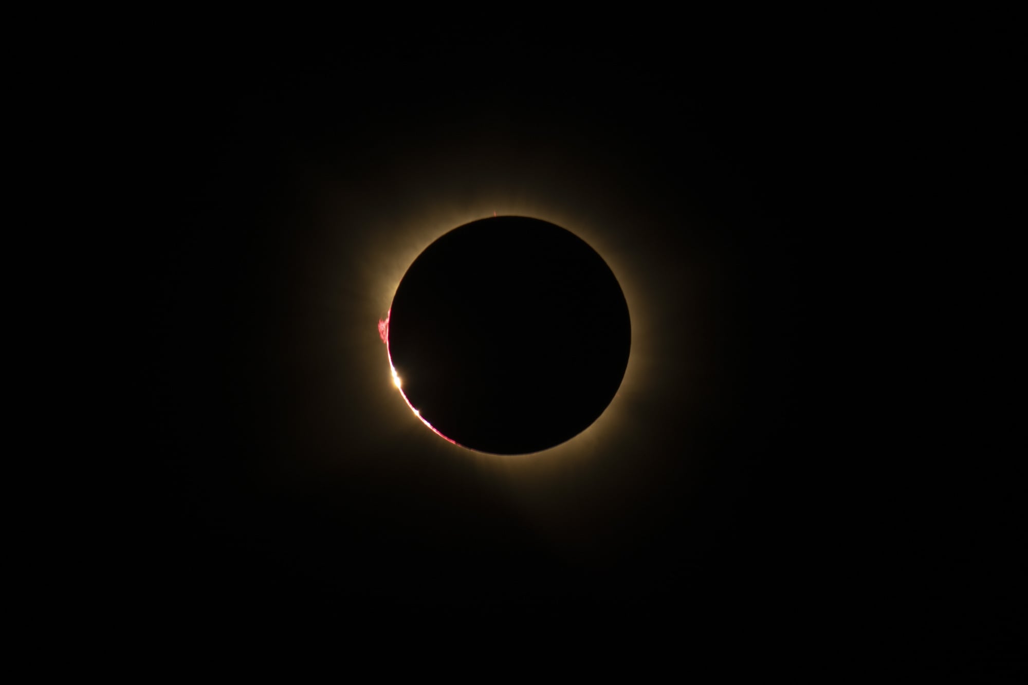 A thin orange corona glows around the pitch black moon.