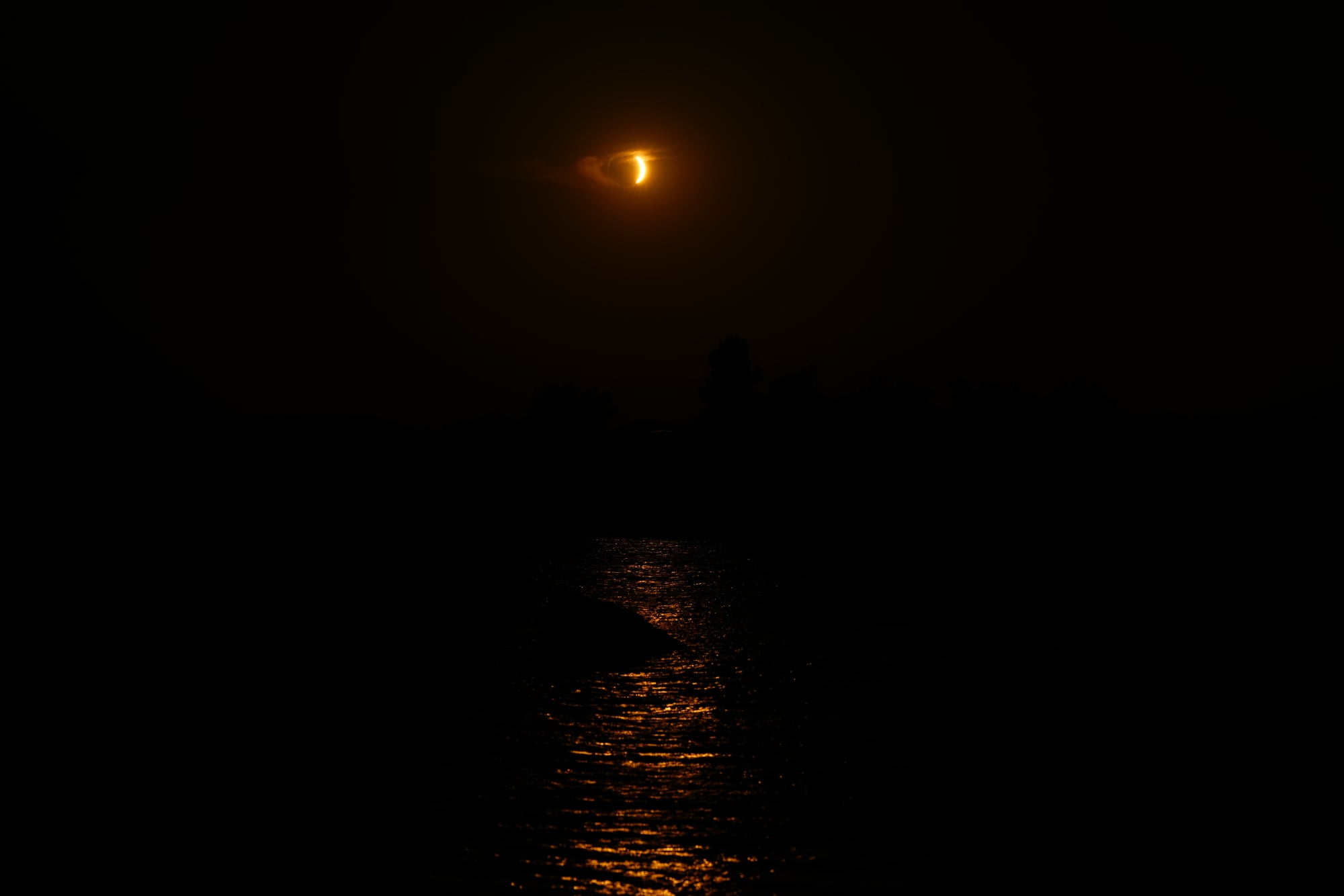 The reflection of the orange glow of the eclipse on a nearly pitch black ocean.