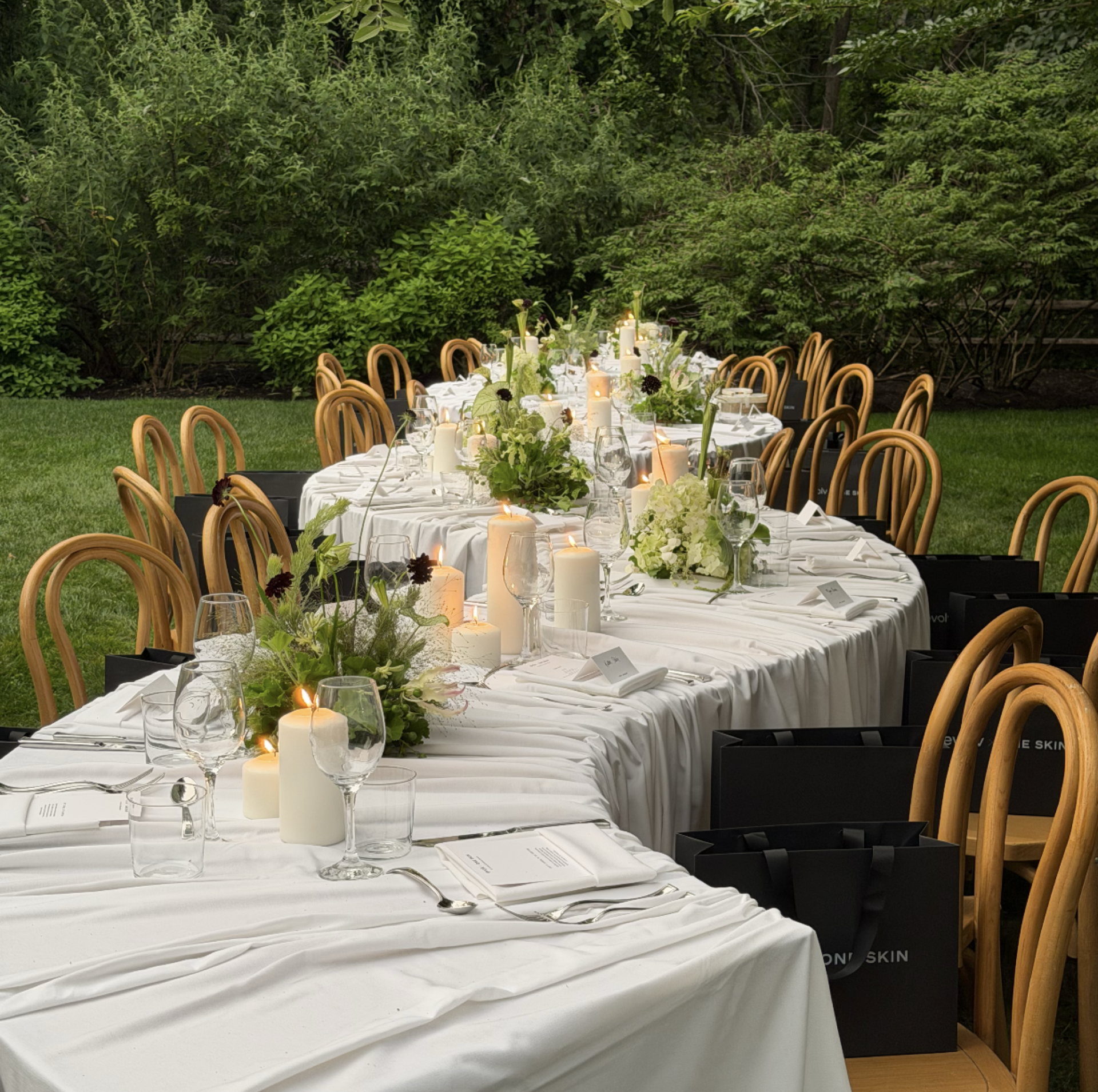 A long curved table with chairs in a grass field for a dinner party