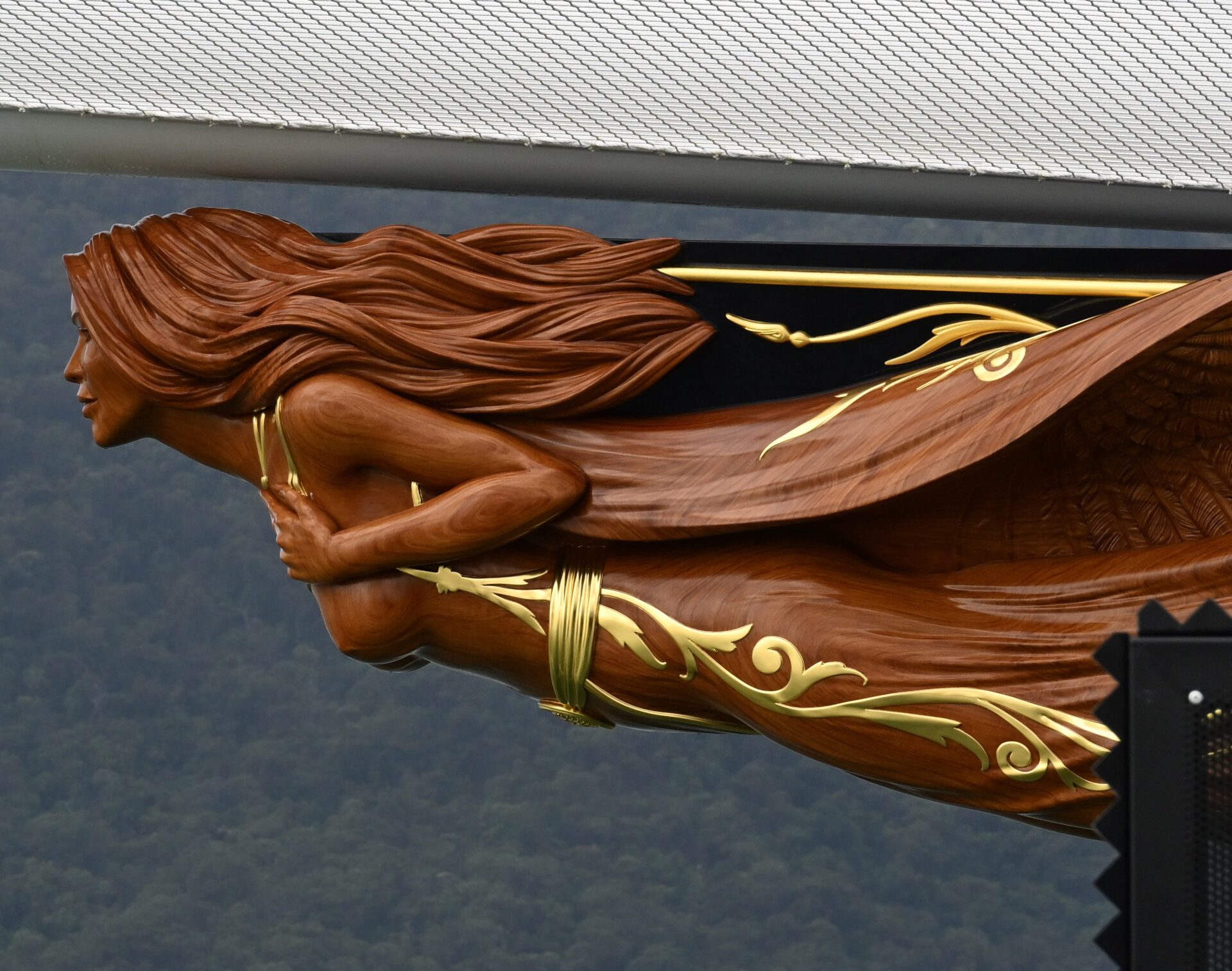 Close-up of a detailed wooden ship figurehead depicting a woman with flowing hair and gold decorative accents on the hull of a superyacht.