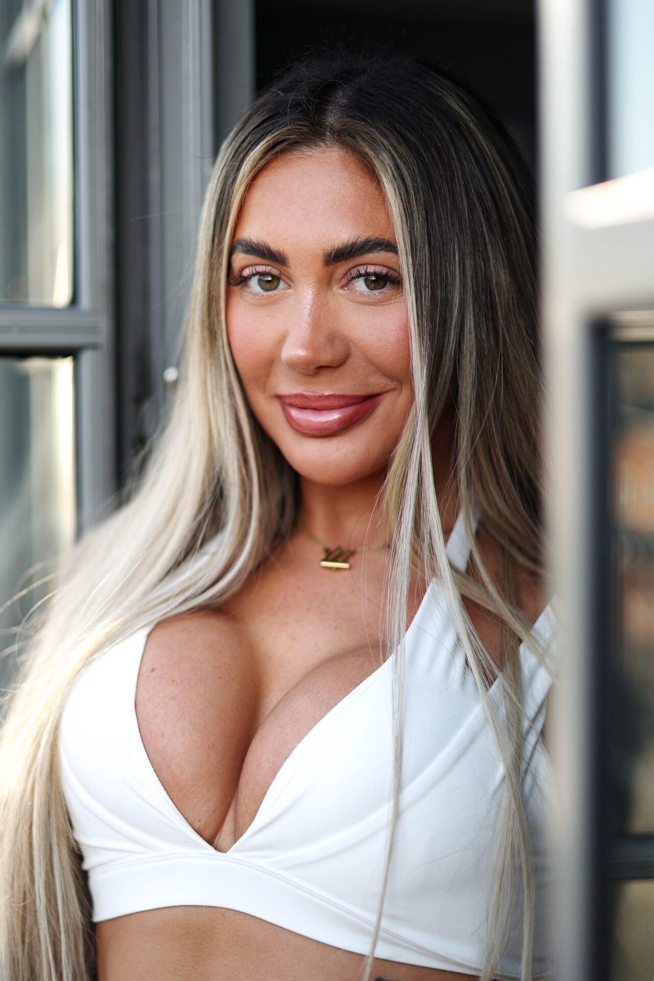 Woman with long dark-to-blonde ombre hair wearing a white plunging crop top, smiling directly at the camera.