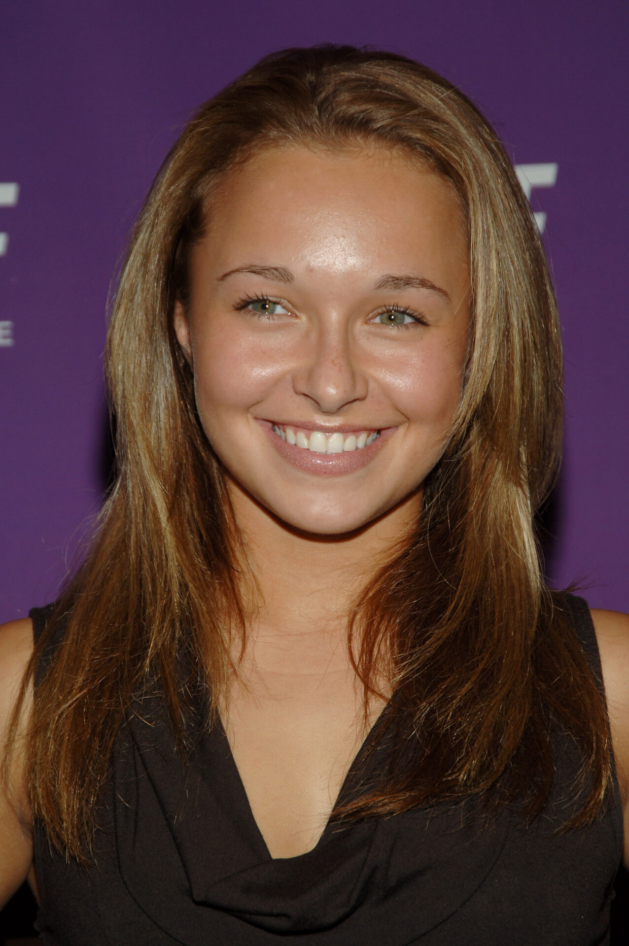 Young woman with long brown hair smiling brightly against a purple backdrop at a New York event.
