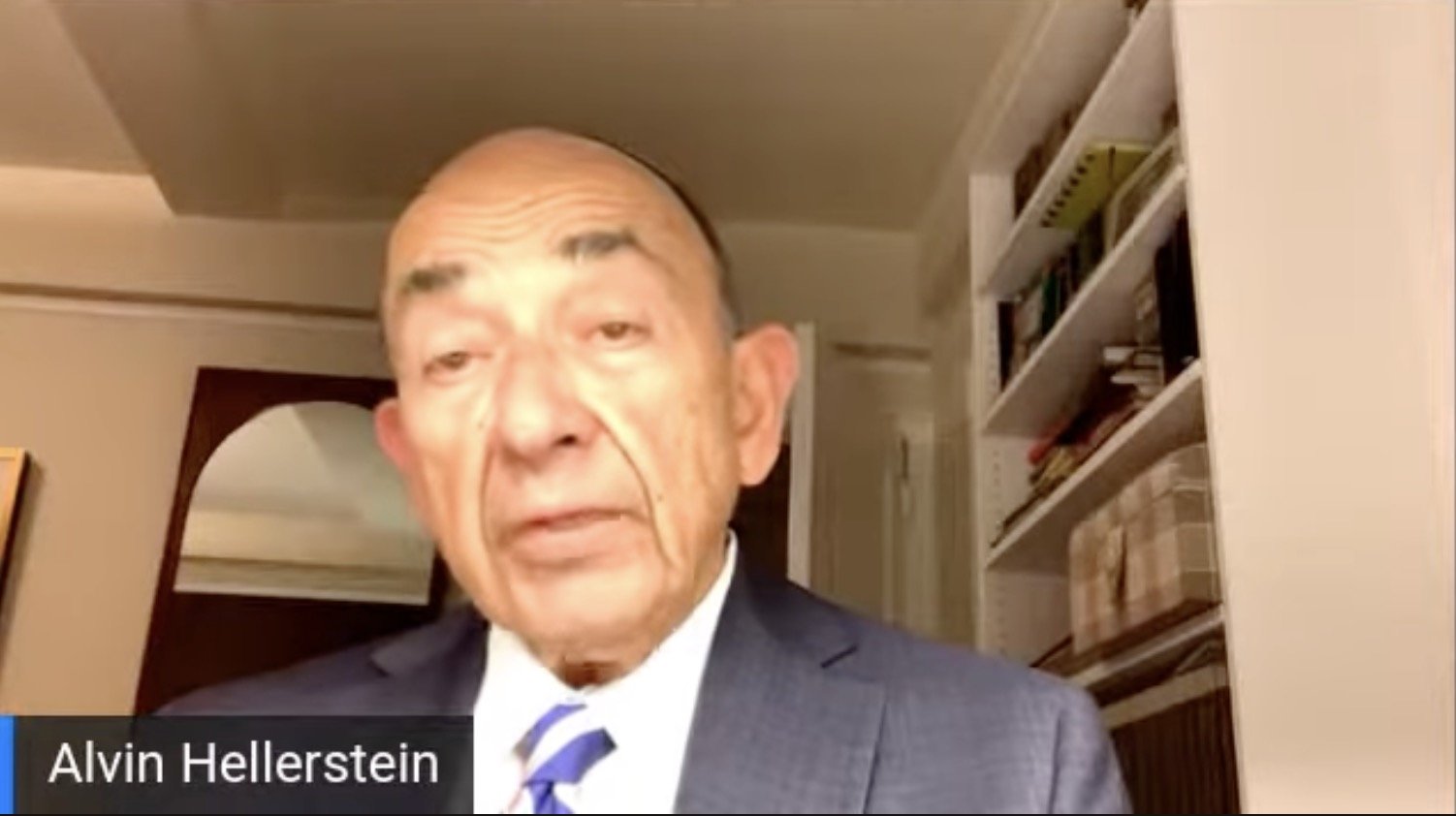 Alvin Hellerstein speaking during a video conference, wearing a suit, with a bookshelf in the background.
