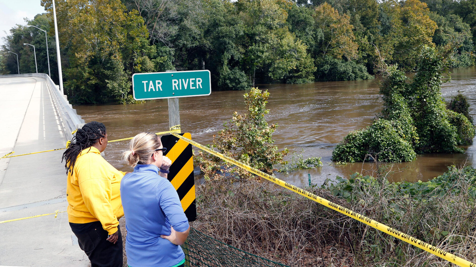 Two women stand next to a river with the road sign 