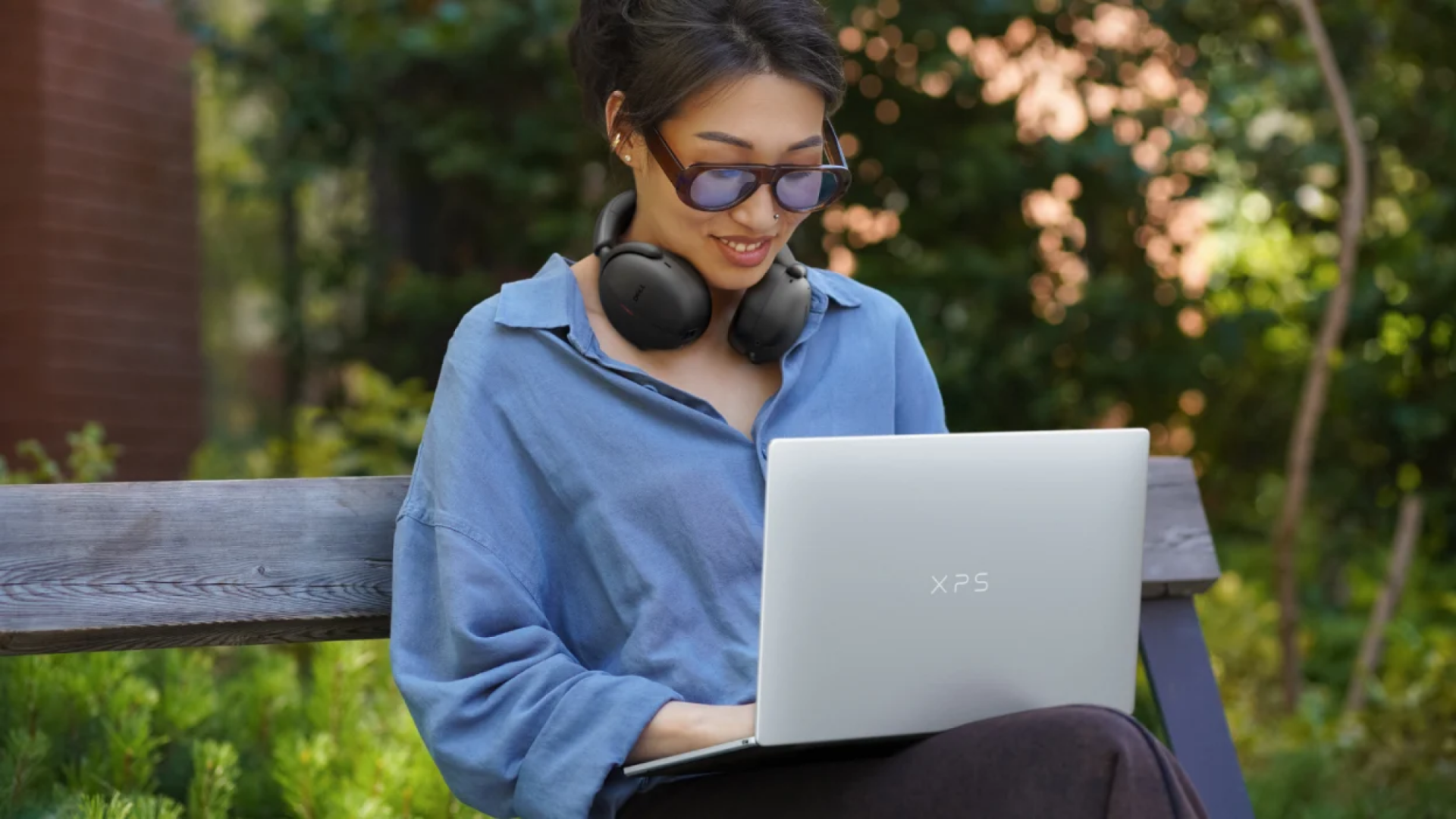 a woman typing on a dell xps 13 while sitting on a bench