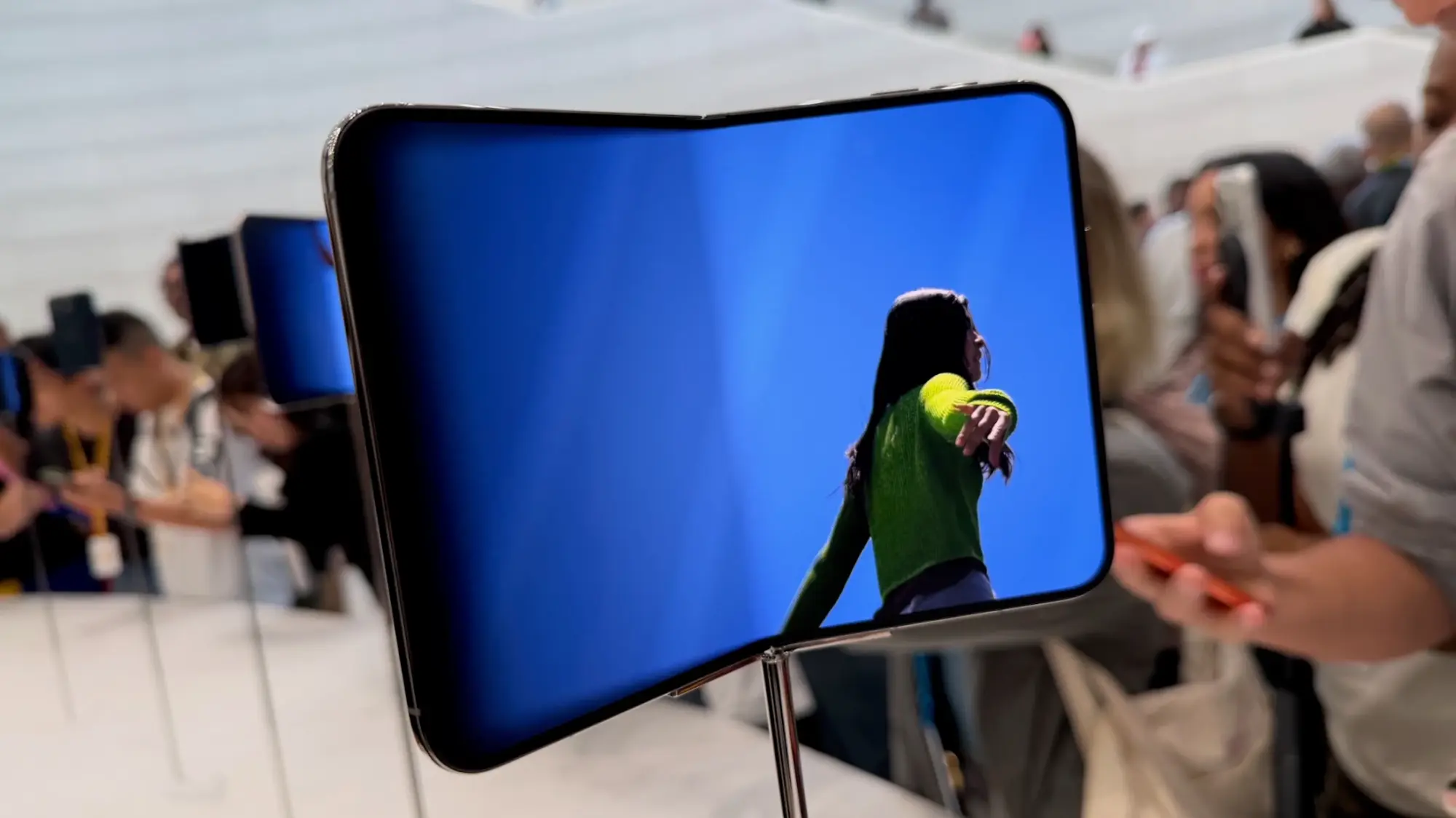 An unfolded iPhone Duo plays a full-screen video of a woman against a bright blue background, with the center crease faintly visible.